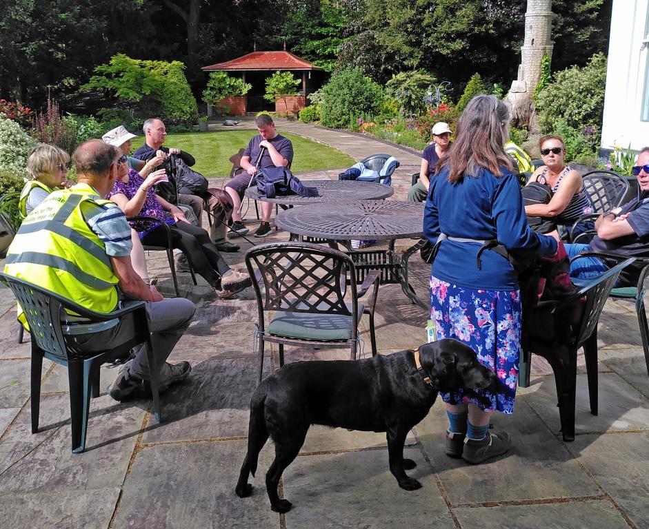 A group of people sits outside with a guide dog in the foreground.