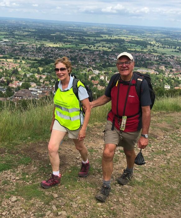 A volunteer guiding a VI man walking on the top of the hills