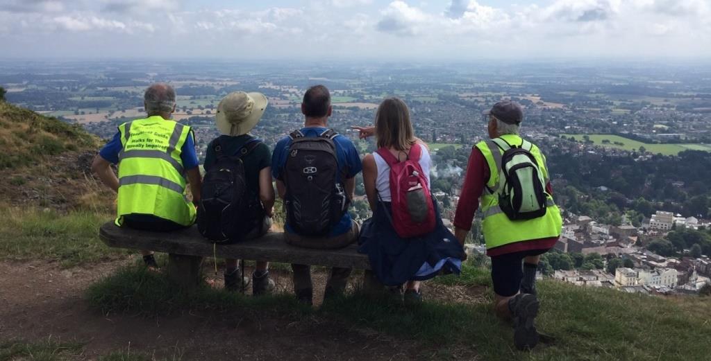 People sitting on a bench with an elevated view of Malvern ahead