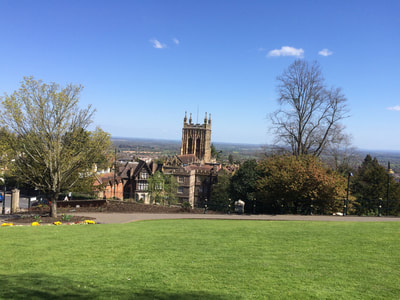 A view of the Malvern Priory tower and Malvern rooftops from the grassy Rose Bank gardens.