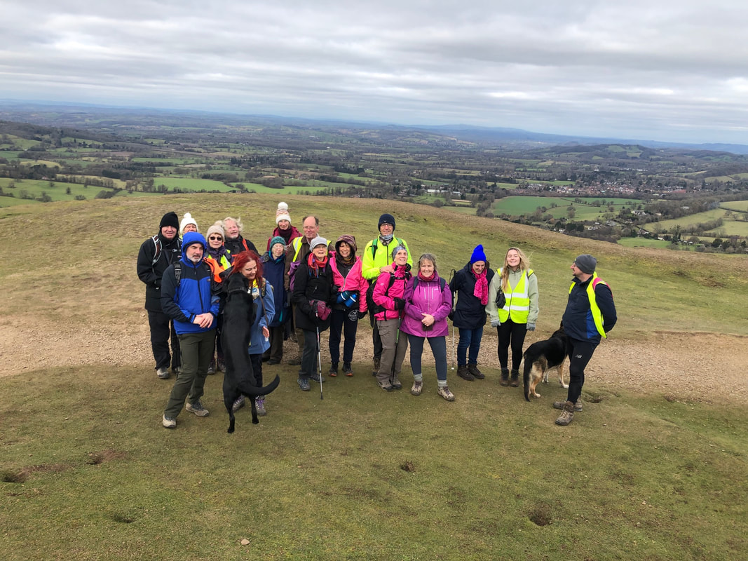 A group of walkers pose for a photo with rolling hills in the Herefordshire valley beyond.